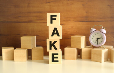Four wooden cubes stacked vertically on a brown background form the word FAKE.