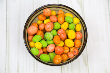 Peanuts in a glaze mix of bright multicolored flowers on a black round plate with a wooden table background. Food is a delicacy snack for beer.