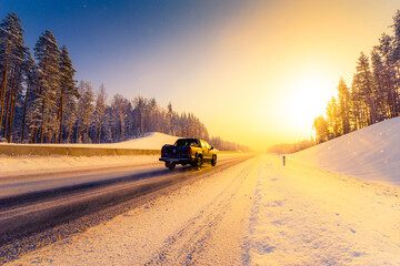 Sunrise on a clear winter morning, pickup rides on the highways in the snow. View from the side of the road. Coniferous forest. Russia, Europe. Beautiful nature.