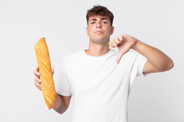 young handsome man feeling cross,showing thumbs down and holding a bread baguette