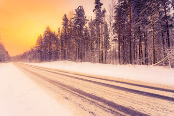 Fototapeta na wymiar Sunrise on a clear winter morning, road passing through the forest in the snow. View from the side of the road. Coniferous forest. Russia, Europe. Beautiful nature.