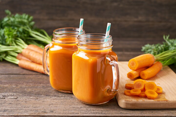 Fresh carrot juice in a mason jar glases and vegetables on a rustic wooden table.