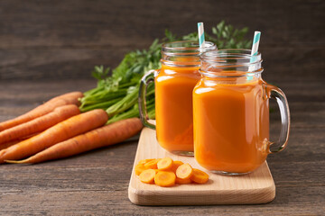 Fresh carrot juice in a mason jar glases and vegetables on a rustic wooden table.