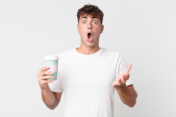 young handsome man amazed, shocked and astonished with an unbelievable surprise and holding a take...