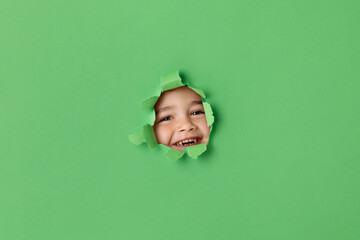 Smiling boy peeking through green torn paper