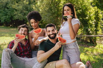 Portrait of multiracial young people eating watermelon outdoor in the countryside and looking at the camera.