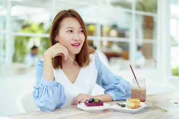 A beautiful Asian portrait is taking a spoonful of cakes on the table and eating them with happy...