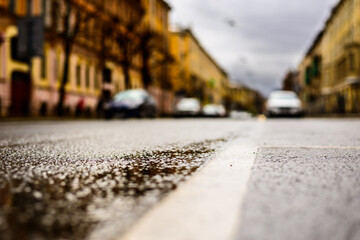 Rainy day in the big city, on an empty road there are parked cars. Close up view from the level of the dividing line