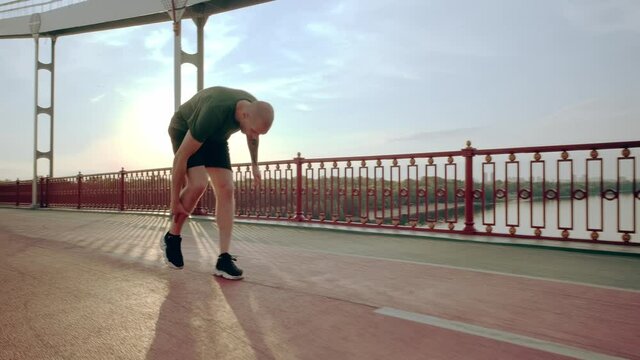 Young runner injured his knee during training. Morning running on the pedestrian bridge in the city at dawn. High quality 4k footage