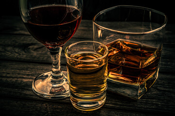Three glasses with brandy, tequila and red wine on an old wooden table. Angle view