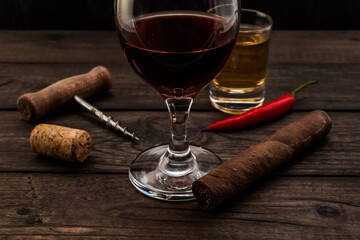 Glass of red wine and tequila with cuban cigar, corkscrew and cayenne pepper on an old wooden table. Close up view, focus on the cuban cigar