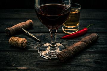 Glass of red wine and tequila with cuban cigar, corkscrew and cayenne pepper on an old wooden table. Close up view, focus on the cuban cigar