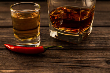 Glass of brandy and tequila with cayenne pepper on an old wooden table. Close up view, focus on the cayenne pepper