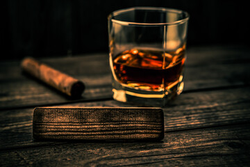 Glass of brandy with cuban cigar and the empty wooden plank on an old wooden table. Angle view, focus on the wooden plank