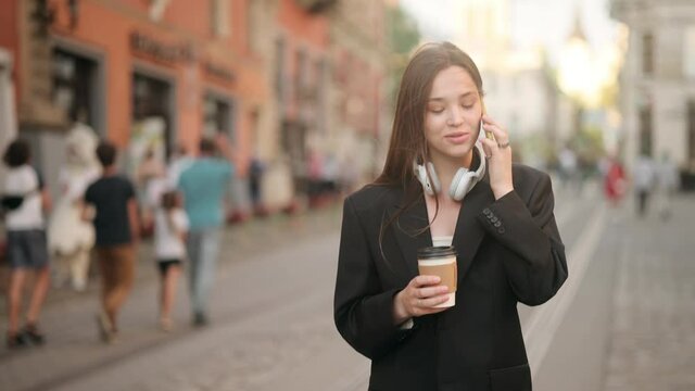 Business woman speaking mobile phone onthe go to office outdoors. Young professional businesswoman walking on city streets and drinking coffee to go