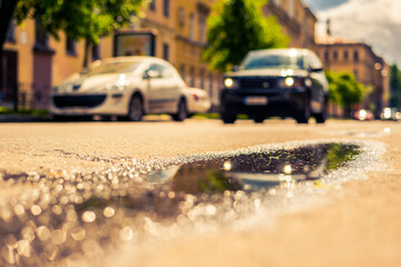 Sunny day after rain in the city, the car rides along the road. Close up view from the level of the puddle on the pavement