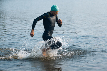 Professional triathlete swimming in river's open water. Man wearing swim equipment practicing triathlon on the beach in summer's day. - obrazy, fototapety, plakaty