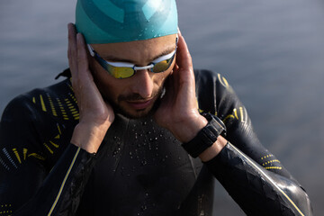 Professional triathlete before swimming in river's open water. Man wearing swim equipment...