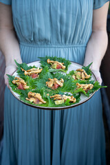 A woman in a blue dress holding a plate of vegan Asian appetizers