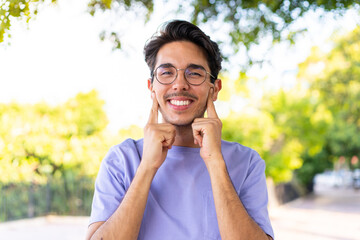 Young caucasian man at outdoors in a park smiling with a happy and pleasant expression