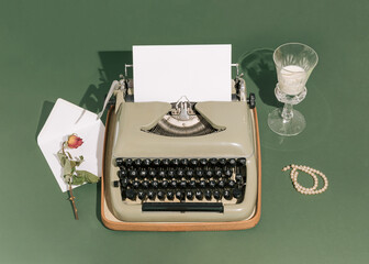 Retro styled scene with a typewriter, white letter, drinking glass, dry rose flower, and pearl bracelet with strong shadows against a green background. Minimal vintage aesthetics. Art direction.