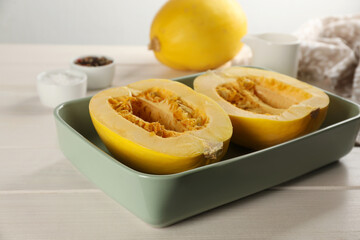Halves of fresh spaghetti squash in baking dish on white wooden table. Cooking at home