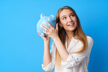 Beautiful smiling young woman with piggy bank on blue background