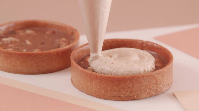 The pastry chef fills a nut tart with mousse on a beige background. Making beautiful desserts. High quality 4k footage