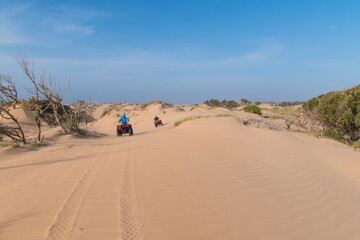 Beautiful sunny day in a desert in Essaouira, Morocco with two quad bike riders driving on the sand