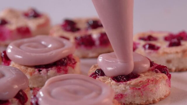 Pastry chef squeezes pink cream from a pastry bag onto the mini cake. Process of assembling mini cake. High quality Full HD footage
