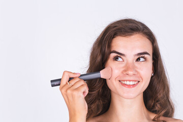 Young beautiful natural soft clean skin woman with freckles light makeup on white background with bare shoulders holding blush brush