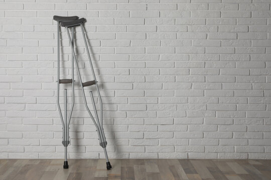 Pair of axillary crutches near white brick wall. Space for text