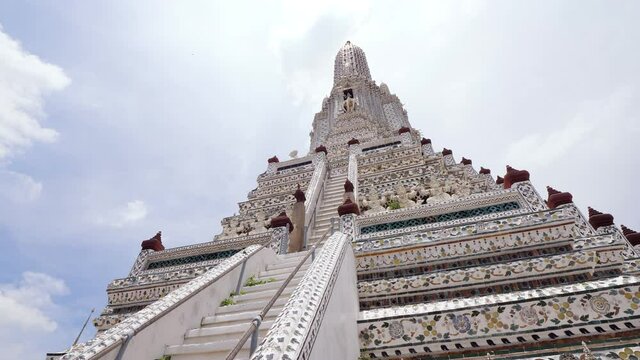 Looking up to decorated Wat Arun spire, steep stairs running up and demon figures seen at down, fine ornamental details over all tower. Details of beautiful Bangkok sight