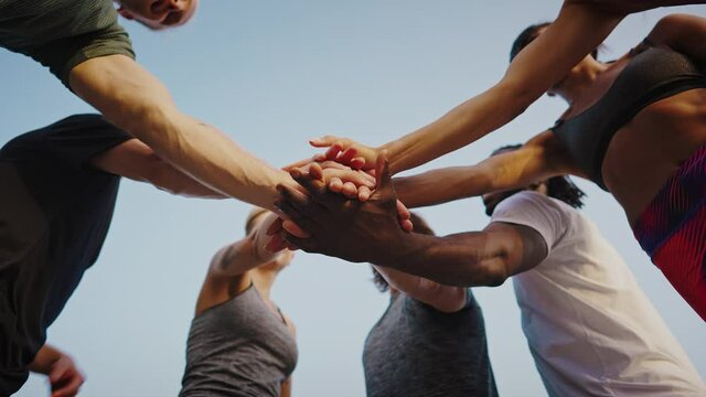 Young beautiful group of sportswomen standing shaking hands after after a successful workout. A team of athletes, men and women, stand in a circle and shake hands. Group of like-minded people