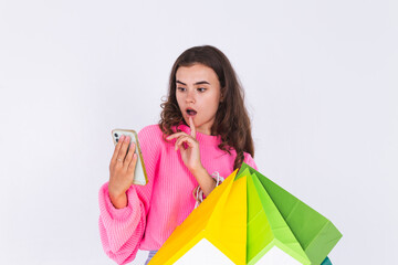 Fototapeta na wymiar Young beautiful woman with freckles light makeup in sweater on white background with shopping bags and mobile phone amazed surprised shocked