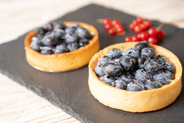 Blueberry tartlet on black plate. Homemade tarts with black berries. Recipe for the blueberry tarts. Bilberry pies.