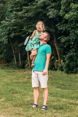 Outdoor vacation dad and daughter. A man holds a child with a tennis racket in his arms 