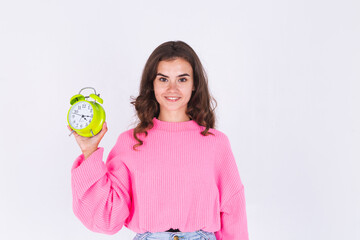 Young beautiful woman with freckles light makeup in sweater on white background with alarm clock positive smiling happy