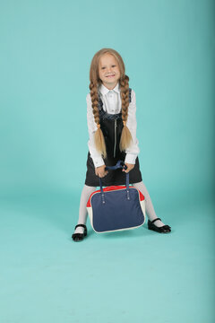 a beautiful little smiling blonde girl in a white shirt and a gray sundress a schoolgirl with a school briefcase in her hands a backpack
