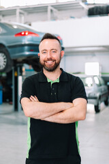 mechanic smiling in uniform is standing on the background of car