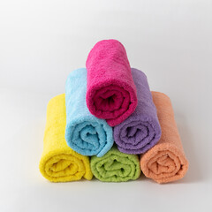 Obraz na płótnie Canvas Colored cotton terry towels for the body on a light background with a cotton branch. Lilac, peach, blue, yellow, light green and burgundy towels, rolled into rolls. Natural textile bath accessories