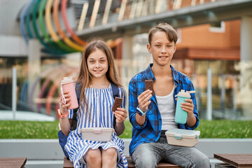 Children boy and girl eating cookies and drink tea after school in park