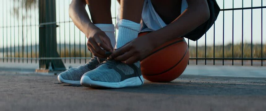 Black African American teenager boy tying shoelaces before playing basketball outdoors. Shot with 2x anamorphic lens