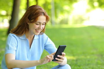 Happy woman using a mobile phone sitting in a park