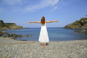 Fototapeta na wymiar Woman in white dress stretching arms on the beach