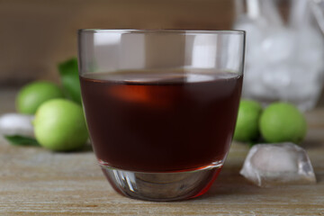 Delicious liqueur with ice and green walnuts on wooden table, closeup