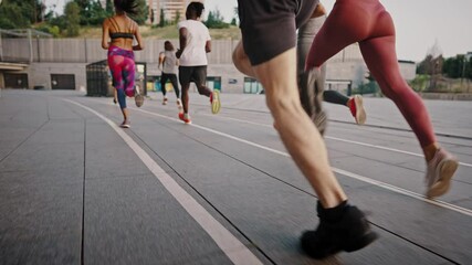 Group of people jogging together at sunrise. Back view of big team of athletes has a group training session on the urban streets of a big city