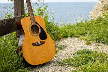 acoustic guitar stands near the fence in the green grass against the background of the sea. music...