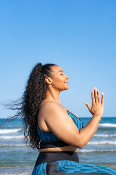 Portrait young female relaxing practicing yoga with namaste on beach