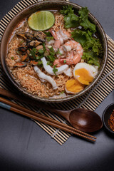 Instant noodles with seafood tom yum, prawns, squid, mussels in a brown ceramic bowl